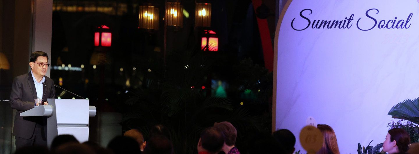 Man at podium speaks to audience; “Summit Social” sign, city view with red lanterns behind.